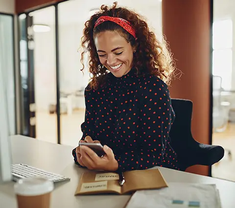 Happy woman sitting at her desk looking at her mobile phone