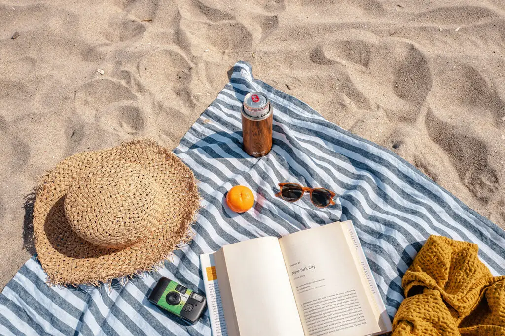 Hat, sunglasses, camera, drink spread out over a towel on the sand at the beach