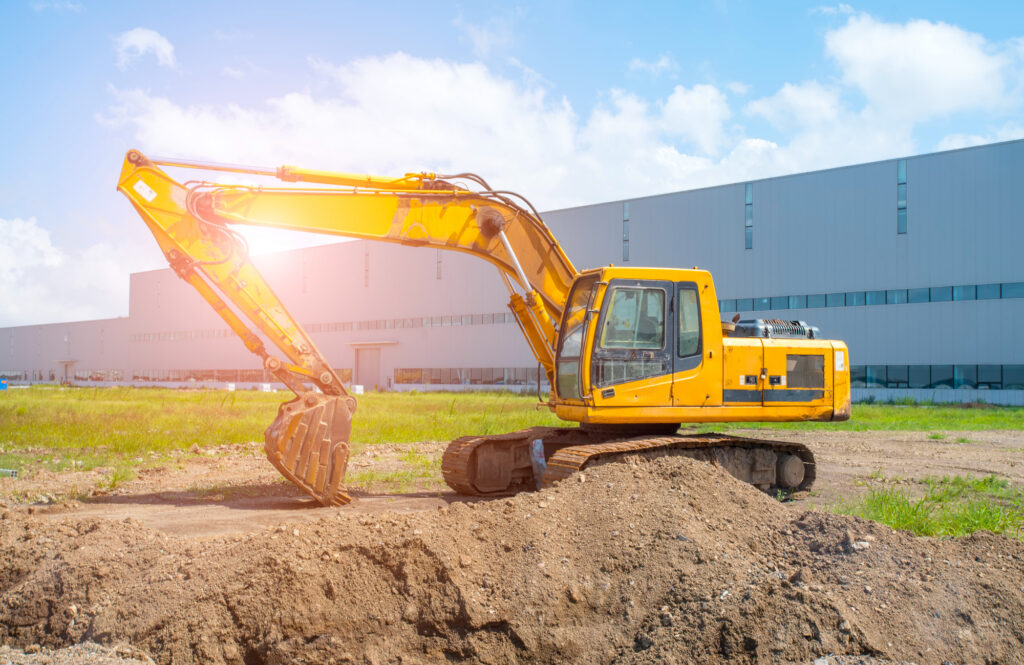 Yellow excavator on building site with commercial building in background
